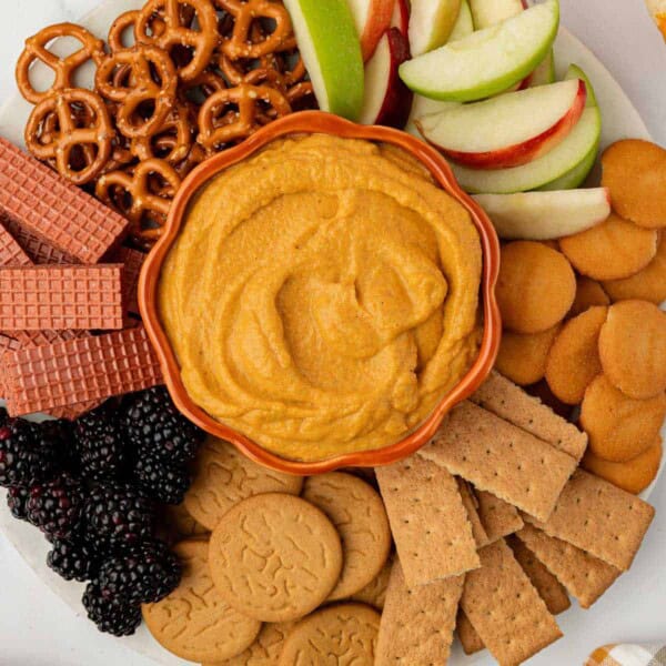 pumpkin dip on a board surrounded with crackers, apples, pretzels, and fruit